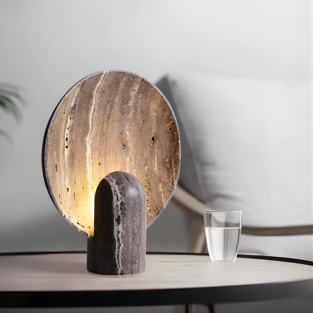 Lámpara de mesa de piedra Solsticia – en travertino oscuro junto a un sofá