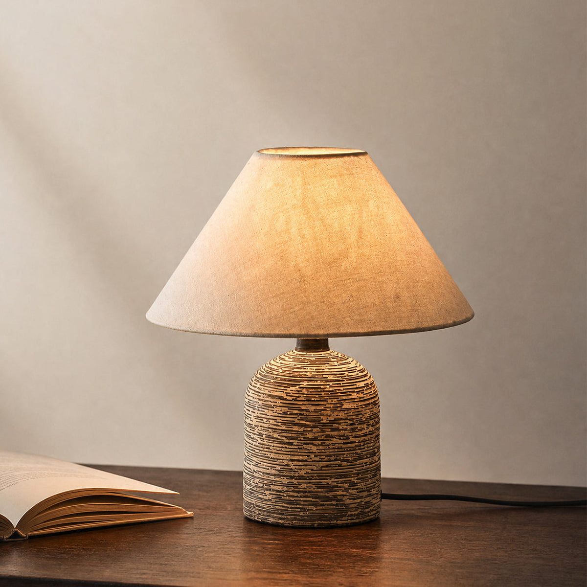Lámpara de mesita de cerámica Terrona – encendida sobre una mesa de madera junto a un libro