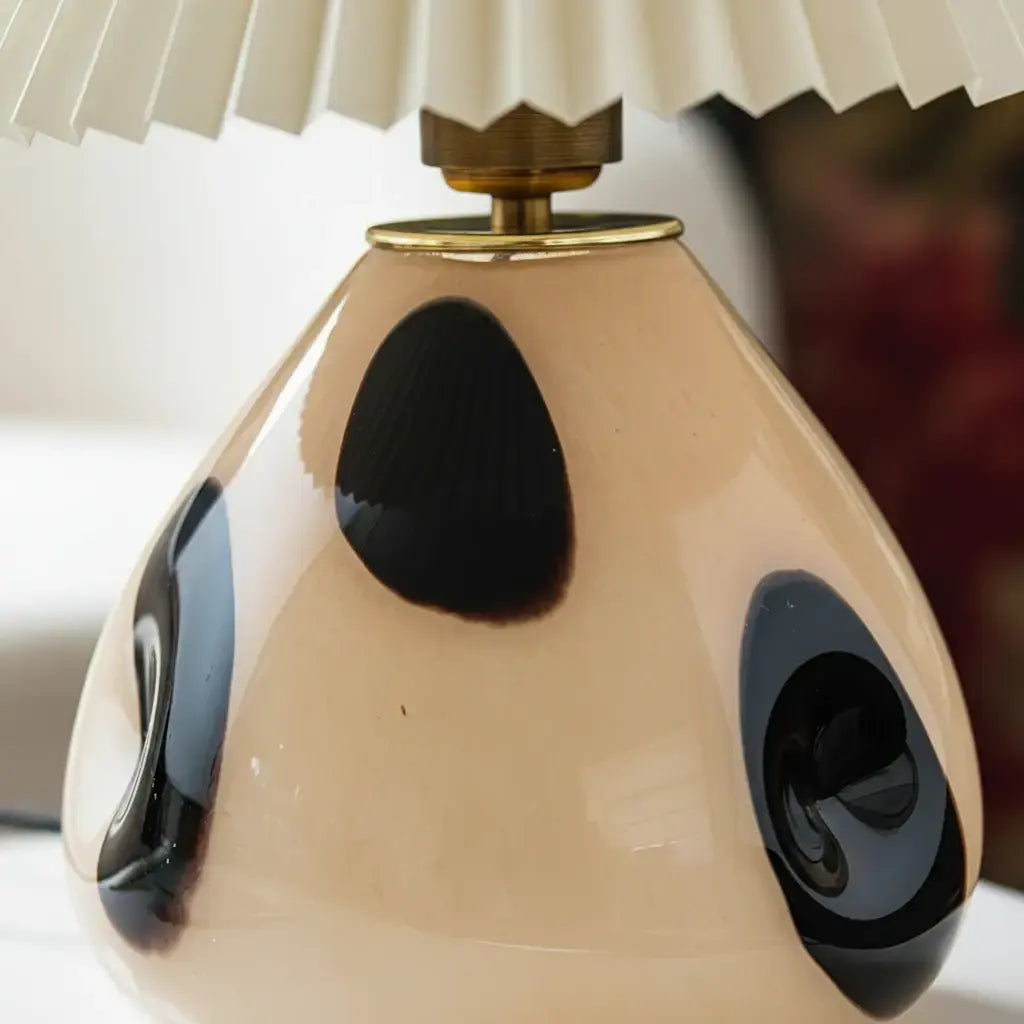 Lámpara de mesa de vidrio con pantalla plisada Tesira sobre una mesa de madera – imagen 13