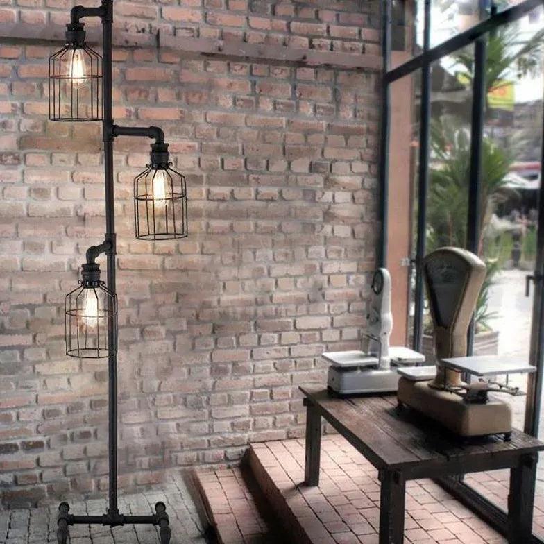 Lámpara de pie industrial de tubería con tres luces Bendora – en una terraza acristalada con pared de ladrillo