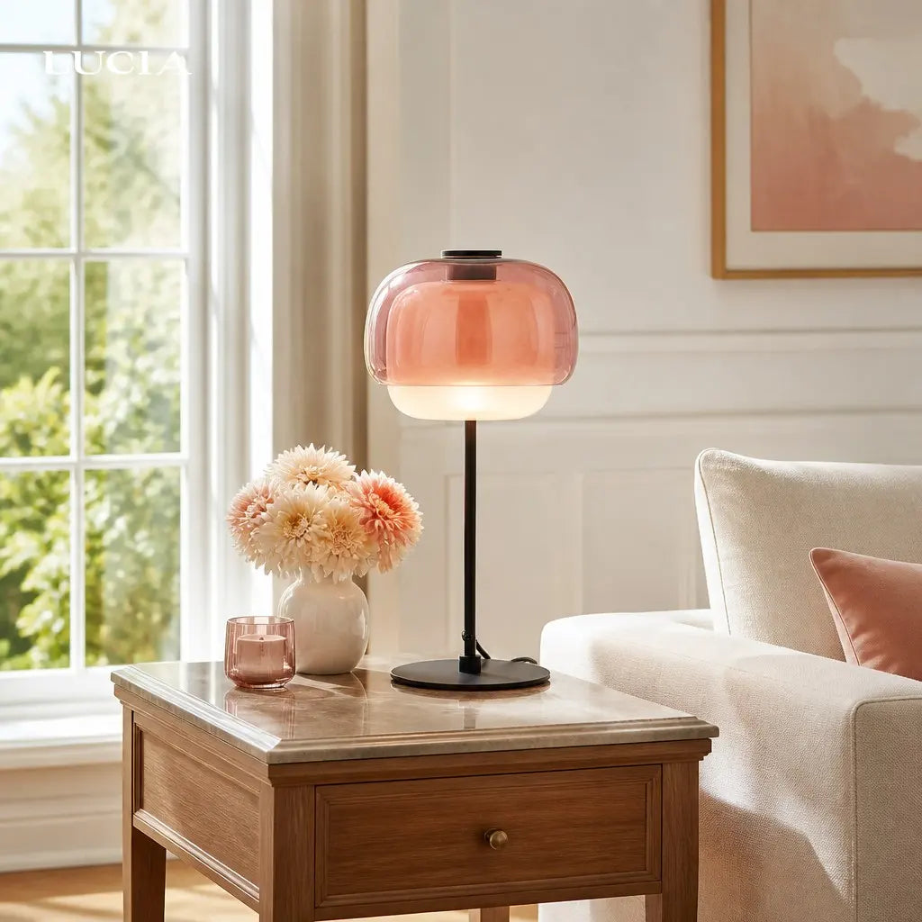 Lámpara de mesa de cristal de color Tinova – rosa sobre una mesa auxiliar de madera