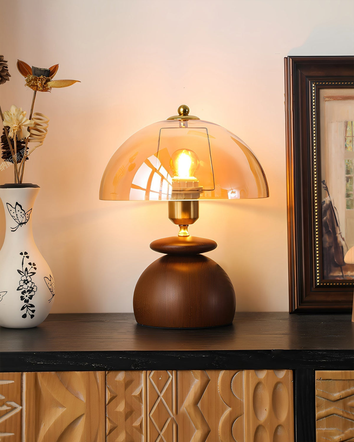 Lámpara de mesita de madera Tostana – encendida sobre un mueble oscuro junto a un jarrón