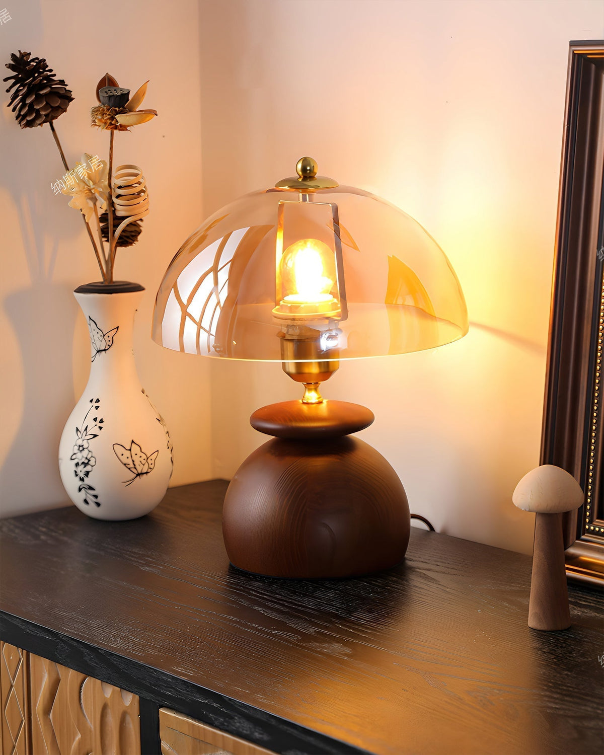 Lámpara de mesita de madera Tostana – encendida junto a un jarrón con flores secas