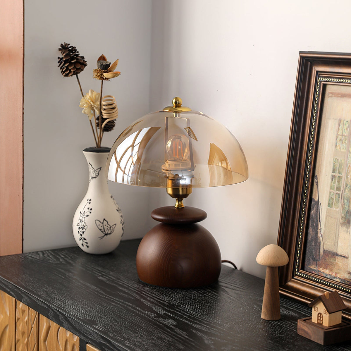 Lámpara de mesita de madera Tostana – encendida sobre una cómoda junto a un marco