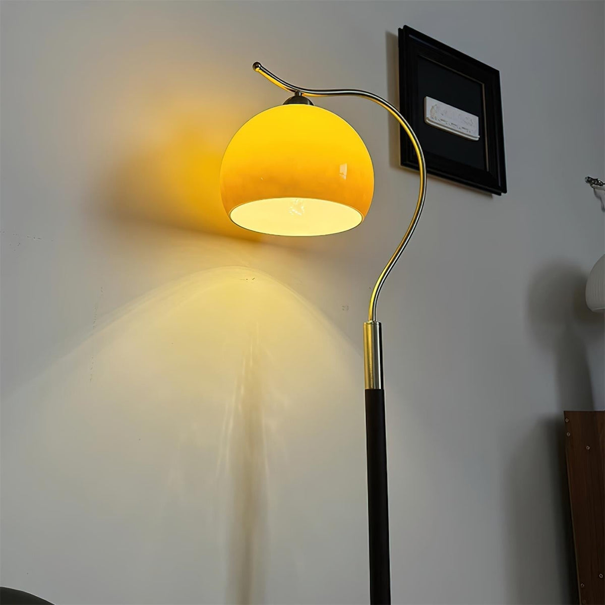 Lámpara de pie con globo de cristal Tostina – encendida con luz cálida sobre la pared