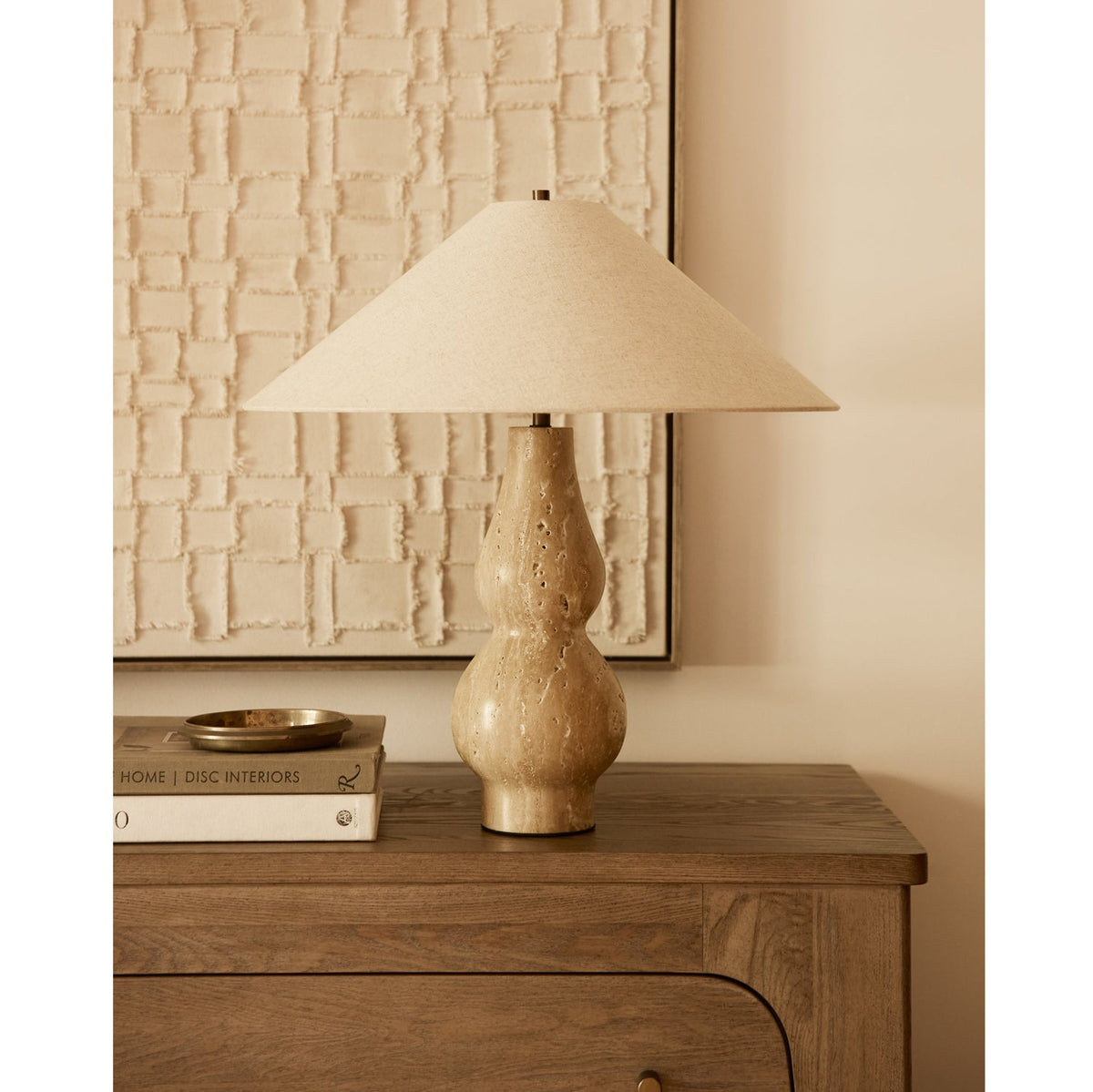 Lámpara de mesa de travertino Travia – sobre una cómoda junto a un cuadro de relieve