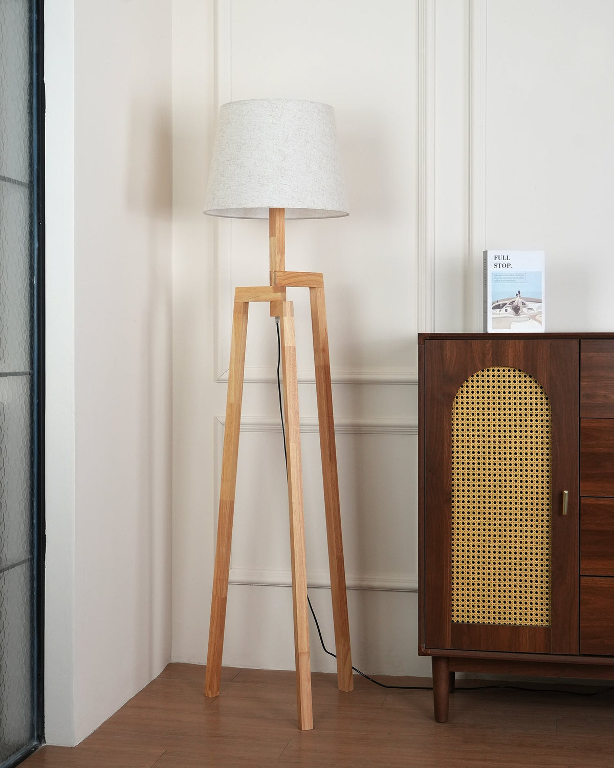 Lámpara de pie trípode de madera Tresalba – junto a un aparador con puerta de rejilla
