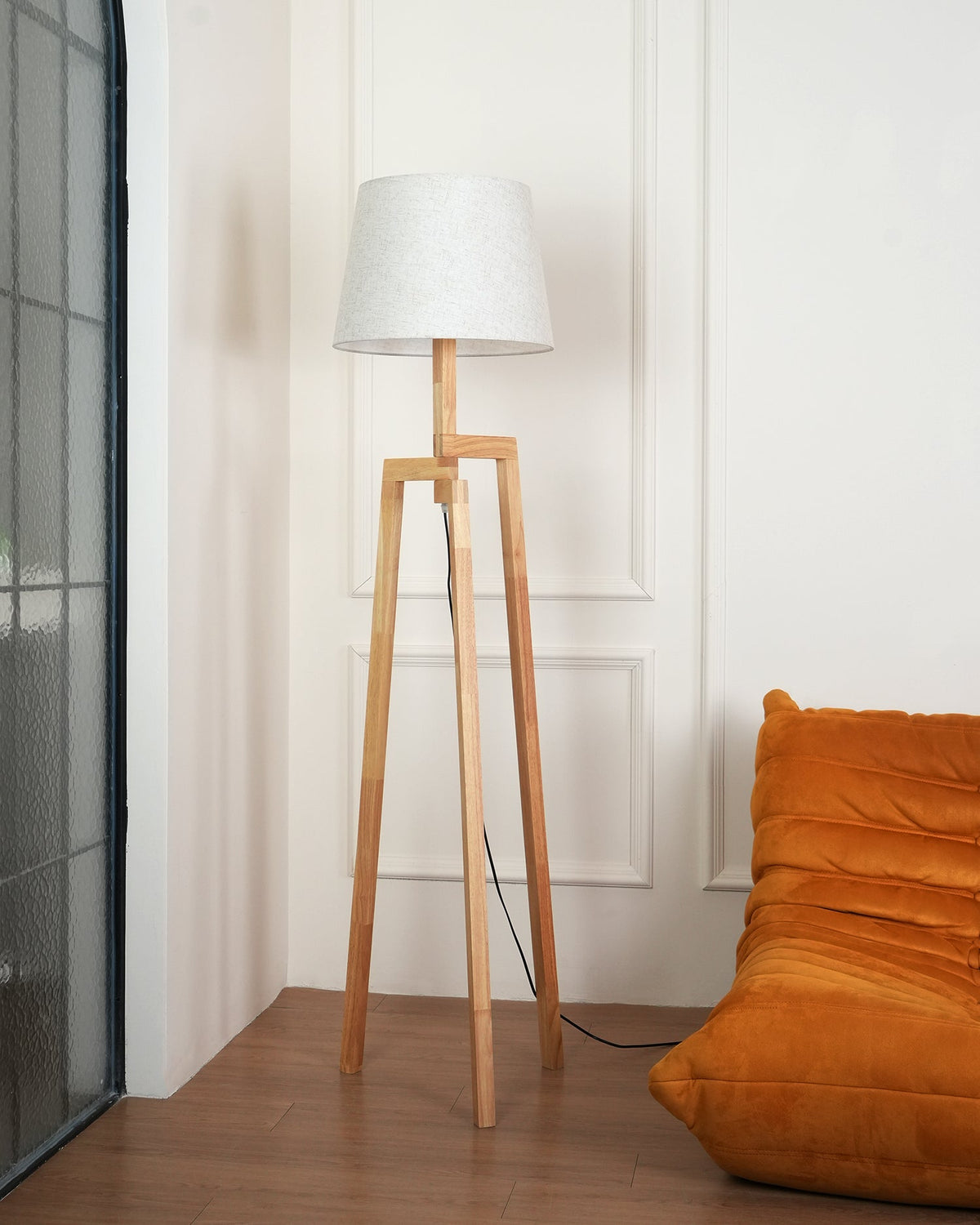 Lámpara de pie trípode de madera Tresalba – junto a un sillón naranja