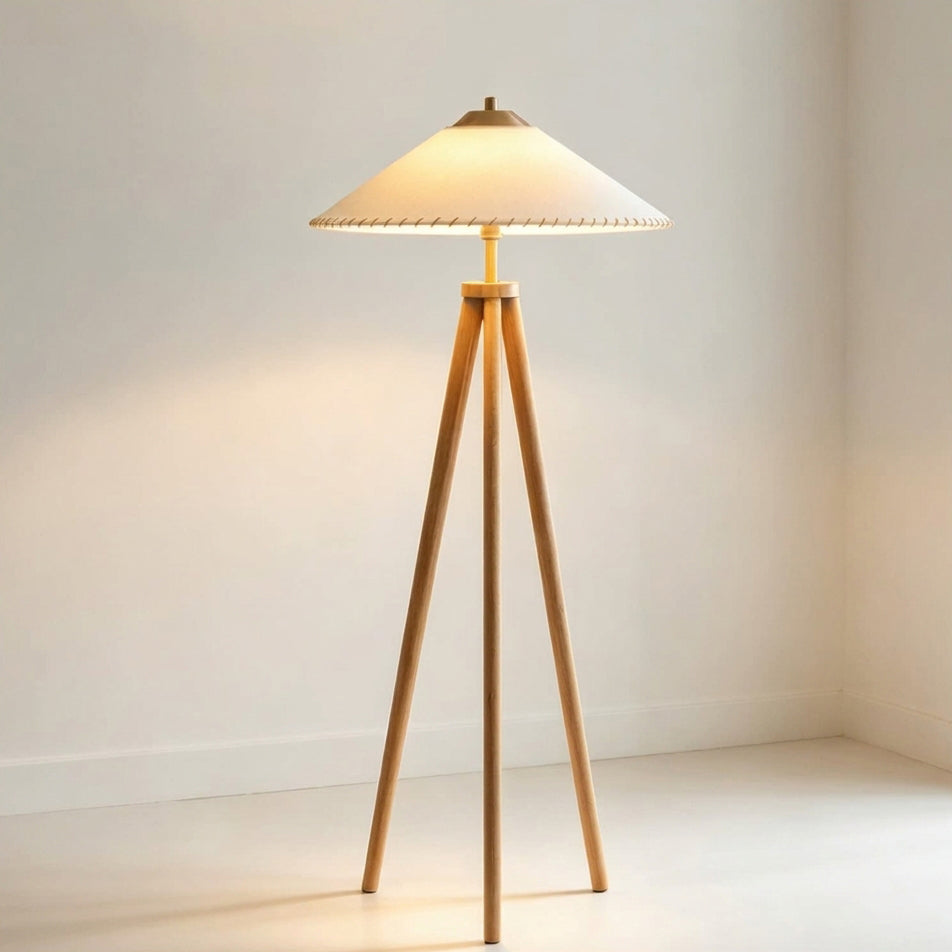 Lámpara de pie trípode de madera Tripela – encendida junto a una pared blanca