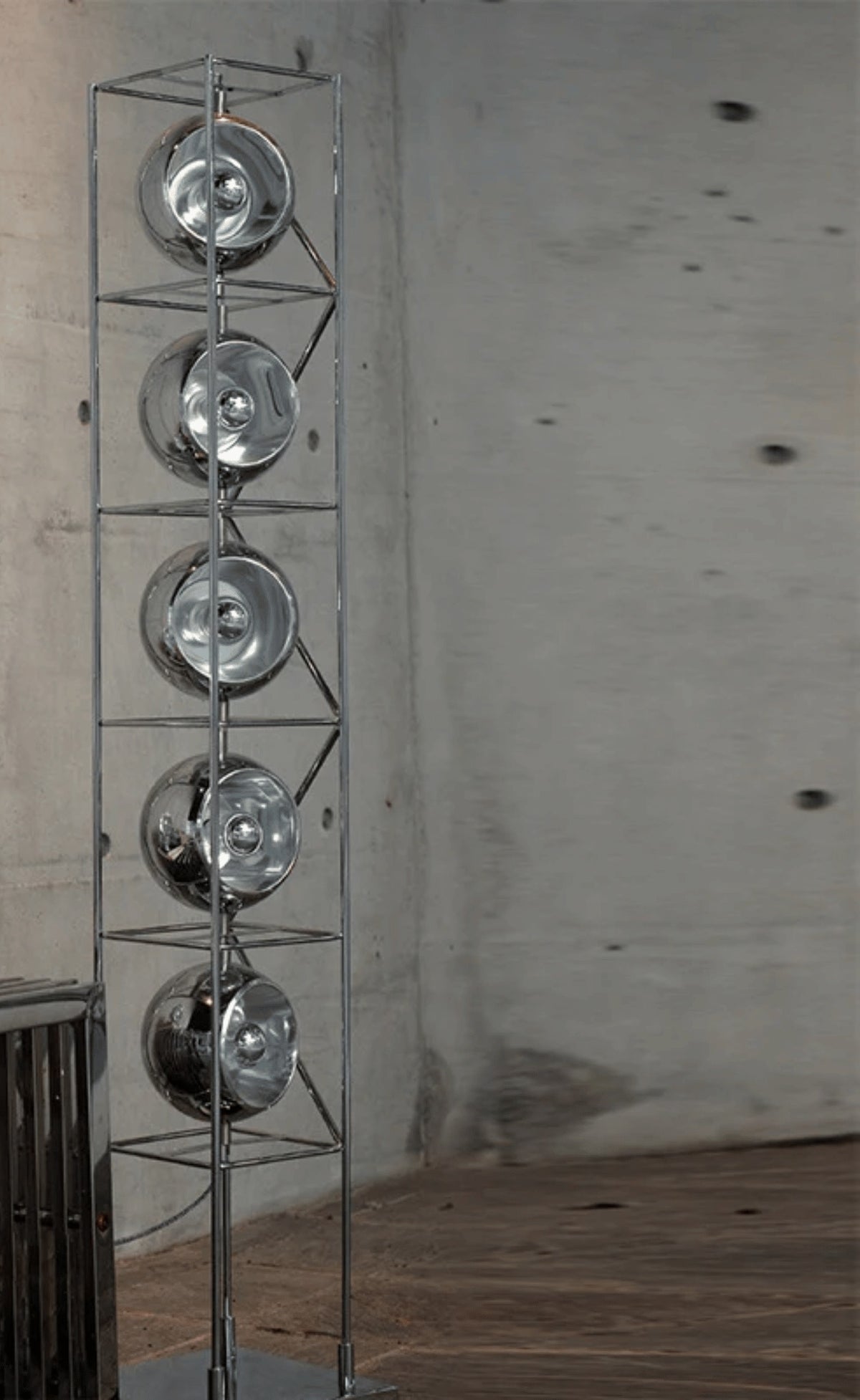 Lámpara de pie torre Urcina con esferas de luz – en cromado sobre una pared de hormigón