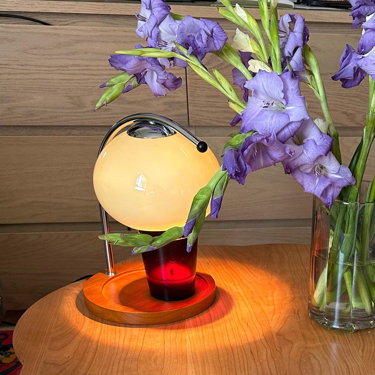 Lámpara calentador de velas Velunda – encendida con una vela roja junto a unas flores