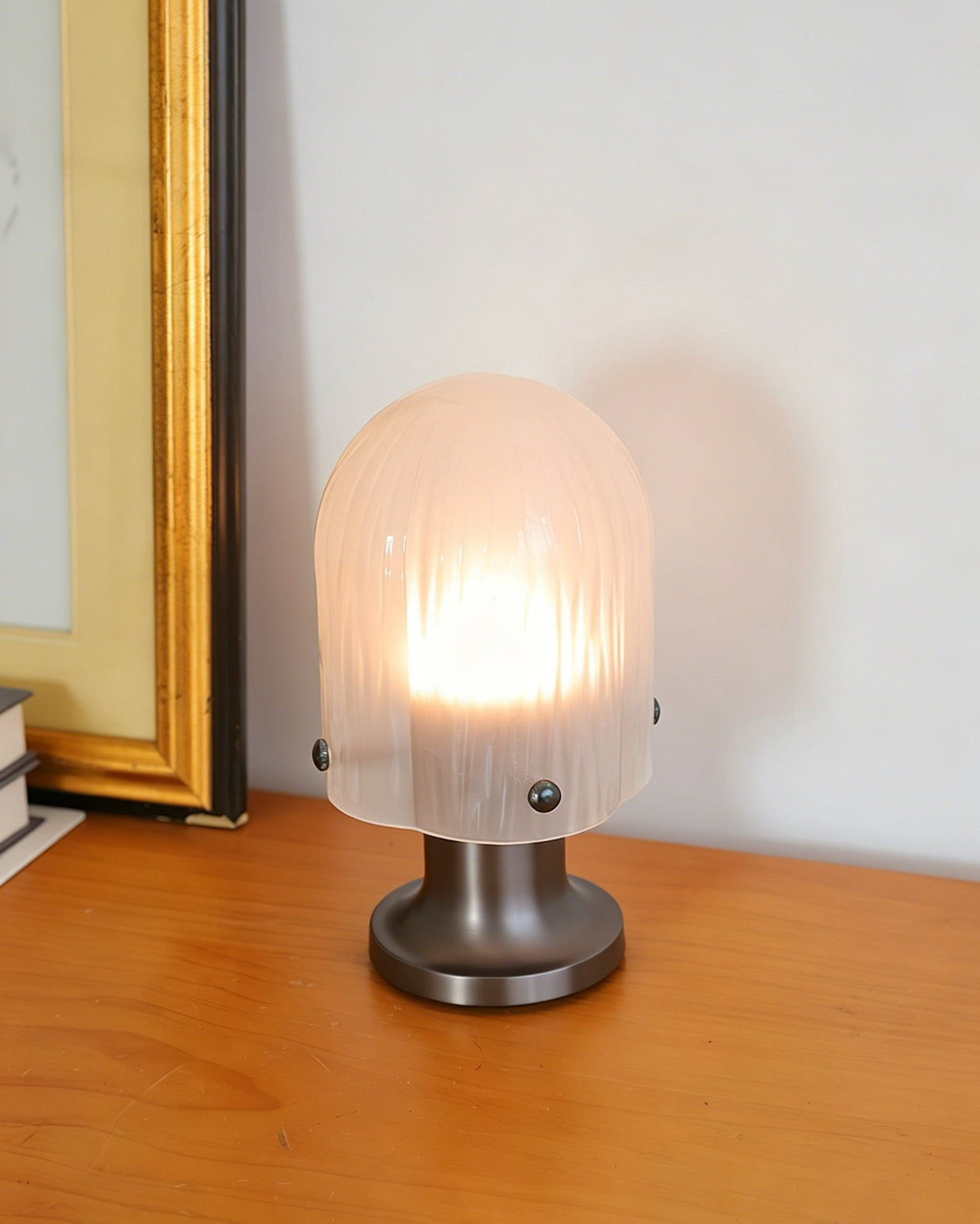Lámpara de mesa de cristal Velundra – con luz cálida junto a un cuadro