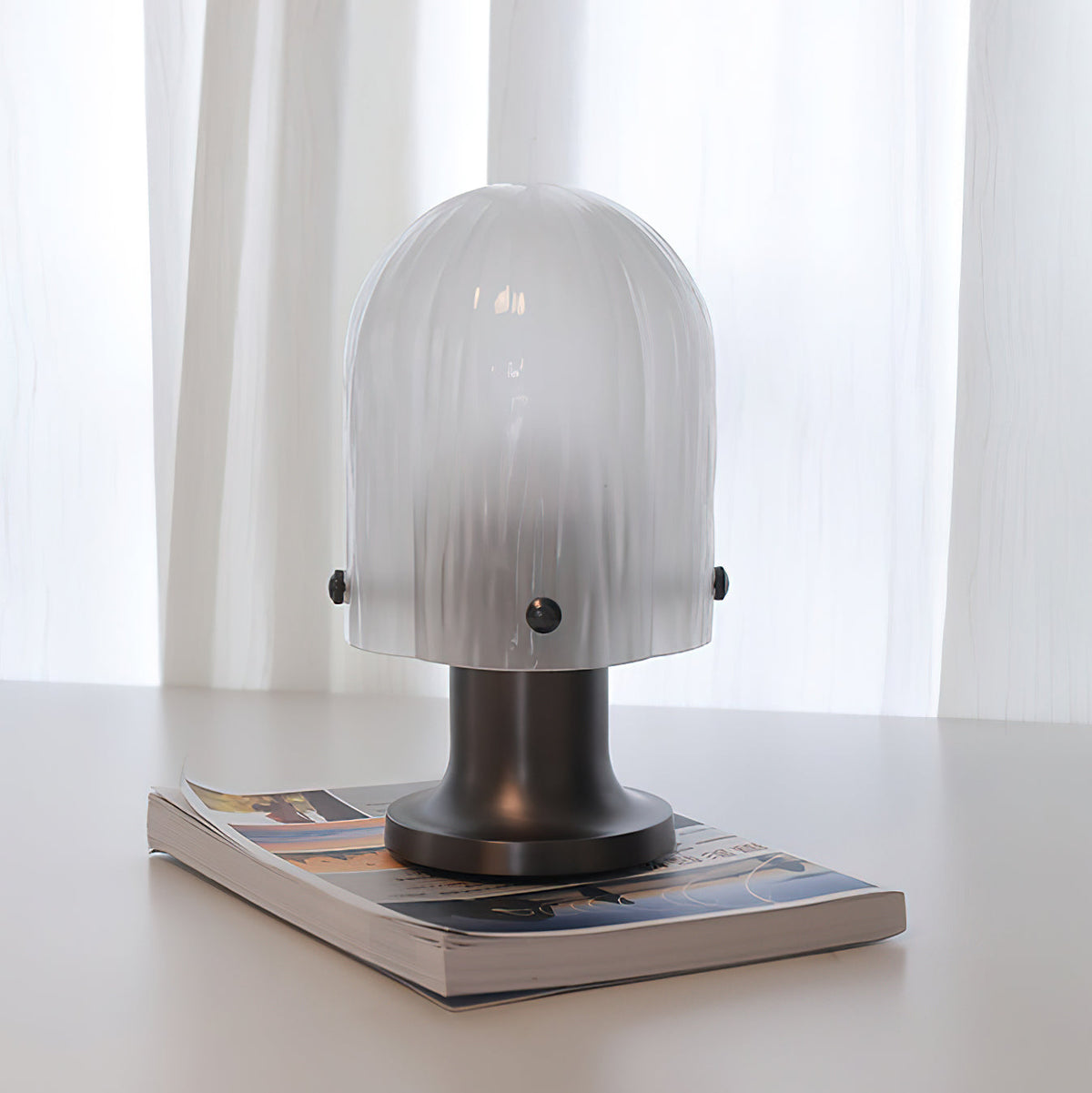 Lámpara de mesa de cristal Velundra – sobre una revista
