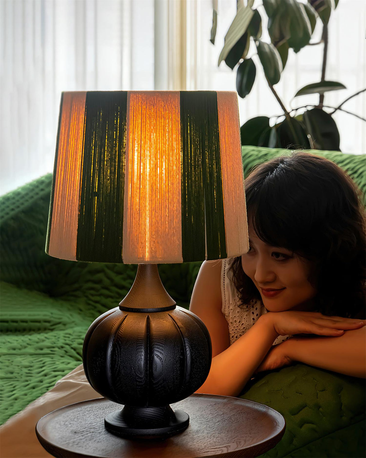 Lámpara de mesa de madera a rayas Vetora – encendida junto a un sofá verde