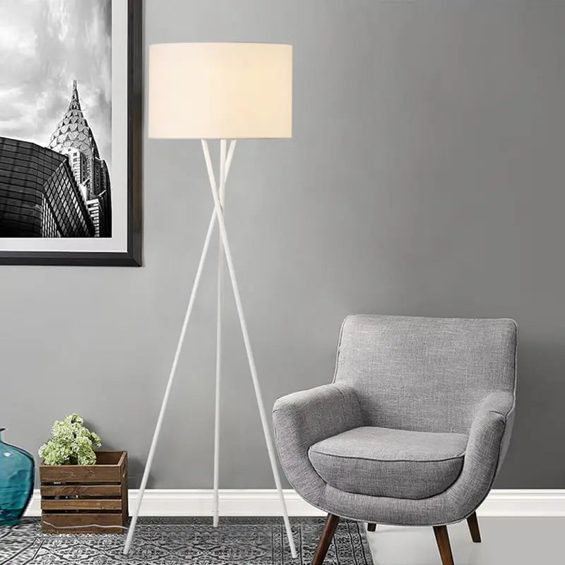 Lámpara de pie trípode nórdica Velatri – en blanco junto a un sillón gris