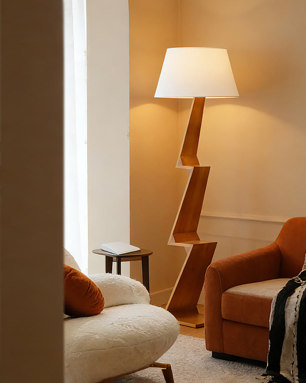 Lámpara de pie de madera en zigzag Zagora – encendida junto a un sillón naranja