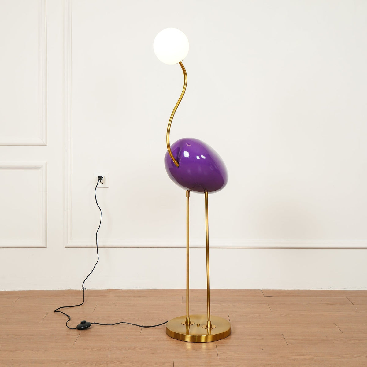 Lámpara de pie pájaro Zancalia – morada con patas doradas junto a la pared