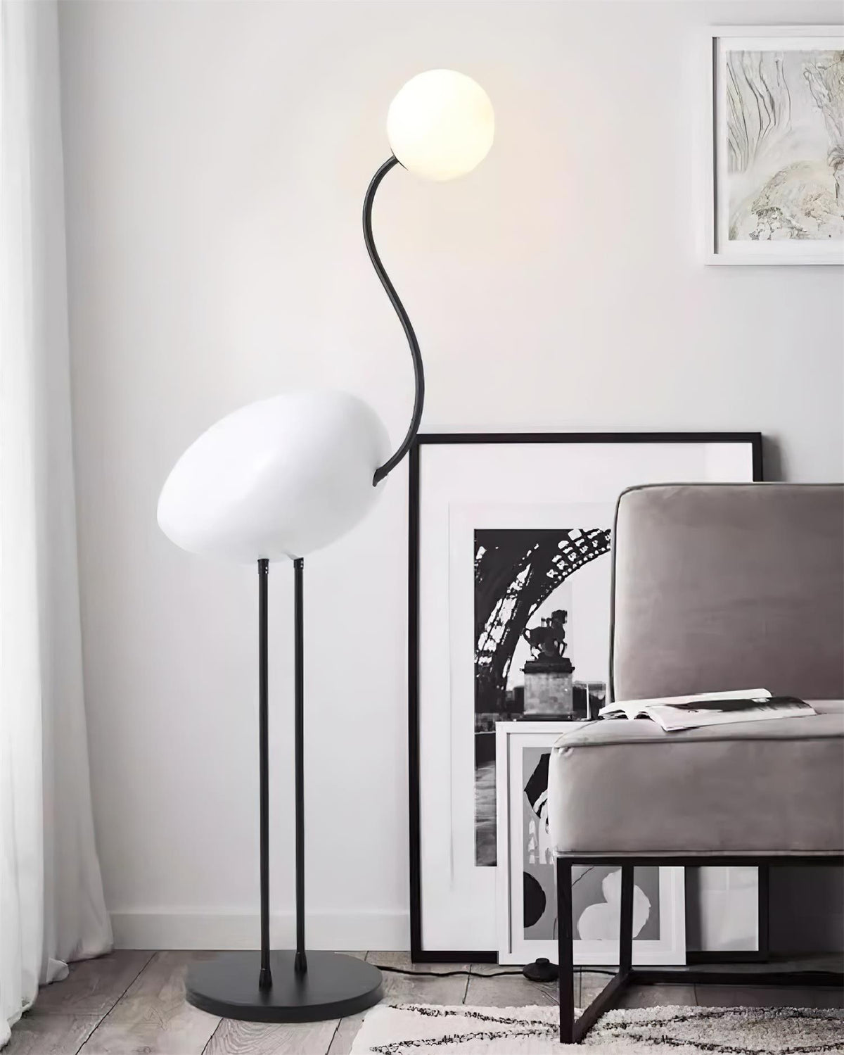 Lámpara de pie pájaro Zancalia – blanca junto a un sillón gris